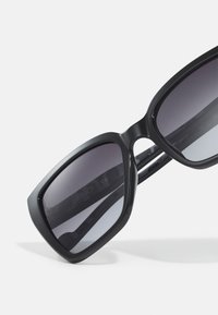 Black oversized sunglasses with a geometric frame, gradient dark lenses, and a smooth texture. Features "LIUJO" branding on the temple.
