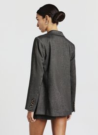 Blazer ajusté gris en tissu texturé, avec un col à revers, des manches longues ornées de quatre boutons décoratifs sur chaque poignet, et une silhouette cintrée.