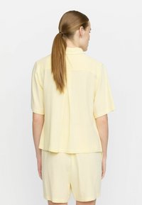 Top giallo a maniche corte realizzato in morbido tessuto, con cucitura a foglia sul retro e vestibilità comoda, abbinato a pantaloni corti coordinati.