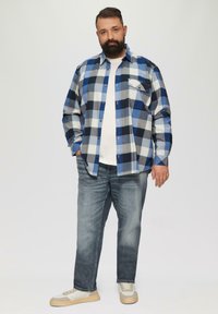 Niebieska i biała koszula flanelowa w kratę z kieszonką na piersi, noszona na białej koszulce. W zestawieniu z jasnoniebieskimi dżinsami i beżowymi sneakersami.