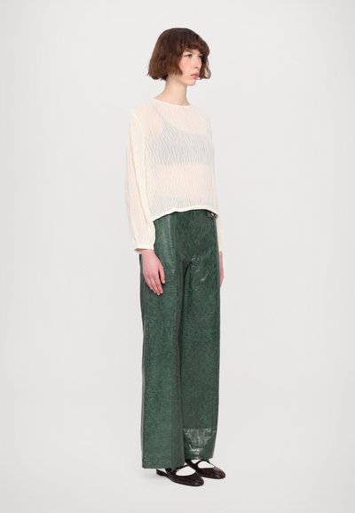 Lätt, genomskinlig off-white långärmad topp i kombination med strukturerade, löst sittande mörkgrön faux läderbyxor. Enkla svarta skor fulländar stilen.