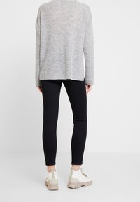 Jasnoszara sweter z dzianiny o luźnym kroju, z okrągłym dołem. Połączony z obcisłymi czarnymi legginsami i beżowymi trampkami za kostkę.