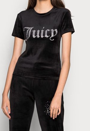 Femme portant un haut à manches courtes en velours noir avec "Juicy" en strass et un pantalon assorti en velours noir avec un motif en strass.