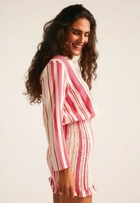 Top de manga larga a rayas rosas y blancas con escote en forma de V, combinado con una falda fruncida en tonos rosa y crema con un dobladillo con volantes.