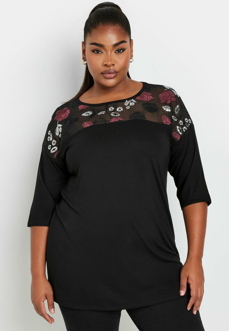 Musta pitkähihainen paita, jossa on läpinäkyvä brodeerattu verkkokaula-aukko, jossa on punaisia ja valkoisia kukkakuoseja. Pehmeä kangas ja rento istuvuus.