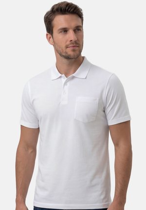 Mężczyzna ubrany w biały polo z krótkim rękawem, kołnierzykiem i kieszenią na piersi, patrzący lekko w lewo.