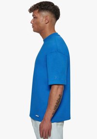 Blå bomulds T-shirt med korte ærmer, rund halsudskæring, med et lille logo på ærmet og en lige kant.