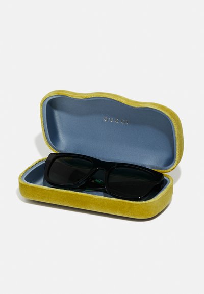 Črne sončna očala v mehkem rumeno-modrem žametnem etuiju; etui ima valovit vzorec in vklesan logotip "Gucci" znotraj.