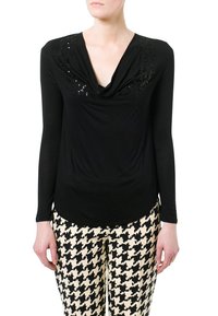 Schwarzes Langarmshirt mit drapiertem Ausschnitt und Paillettenakzenten an den Schultern, kombiniert mit gemusterten Hahnentritt-Hosen in Schwarz und Weiß.