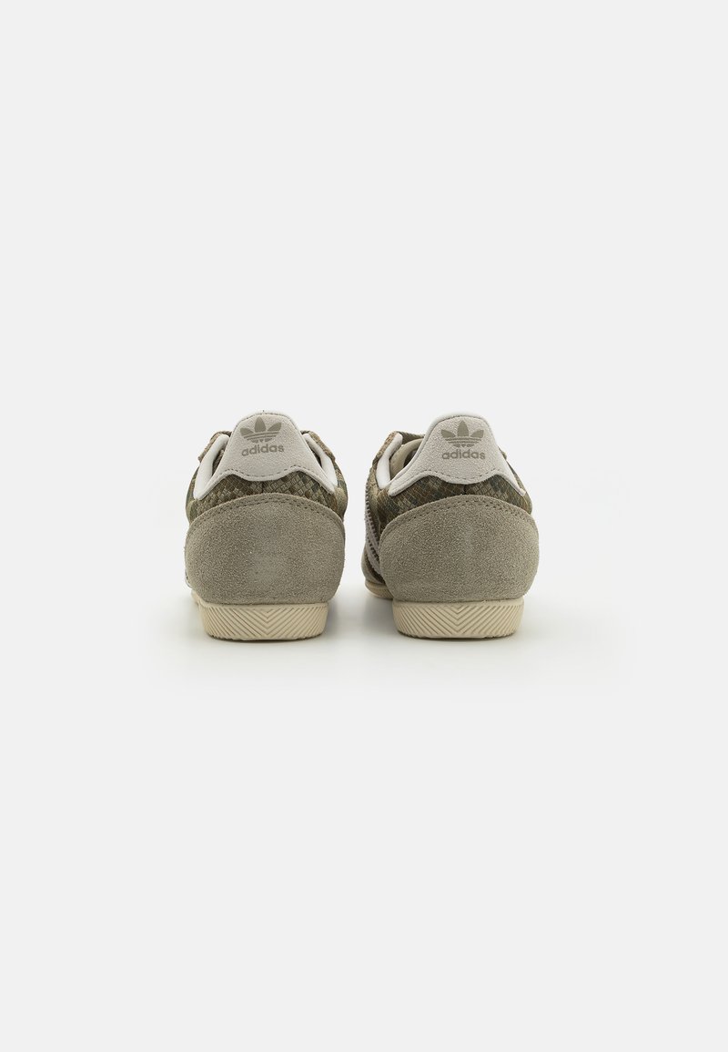 Groene suède sneakers met een gestructureerde bovenkant, voorzien van een lichtgrijze hielpad en een drie-strepen ontwerp, afgerond met een beige rubberen zool.