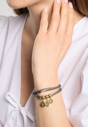 Læderarmbånd i grå med tre gyldne accenter: to runde vedhæng og et stjernevedhæng. Glat tekstur med blank finish.