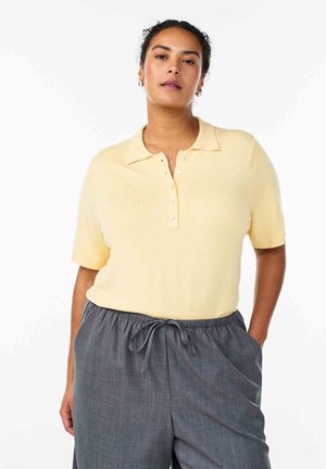 Lysegul polo skjorte med ribbet tekstur, korte ærmer og knaplukning. Kombineret med grå bukser med snøre i taljen.
