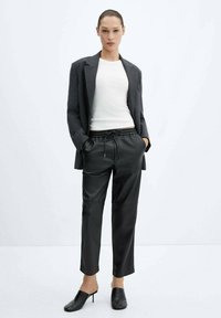 Černé kožené jogger kalhoty s páskem na stažení, spárované s přiléhavým bílým vrškem a šedým blejzrem; elegantní design, hladká textura.