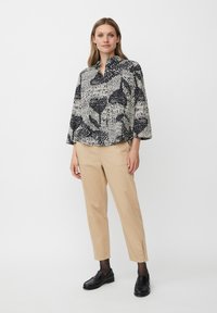 Blusa a fantasia bianco e nero con colletto, maniche a tre quarti, abbinata a pantaloni beige a gamba stretta e mocassini neri.