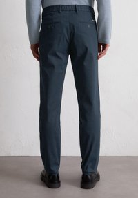 Donkerblauwe broek van zachte stof, met een relaxte pasvorm, een elastische tailleband en twee achterknopen, gecombineerd met zwarte schoenen.