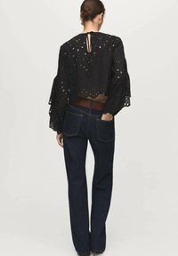Top court en œillets noir avec des manches longues et volumineuses. Il présente des découpes florales et un dos en clé. Associé à un pantalon en denim foncé évasé.
