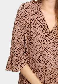 Robe rose avec un décolleté en V, des manches 3/4 avec des volants et une taille froncée. Le tissu présente un motif à pois noirs sur l'ensemble.