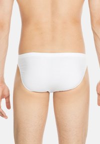 Weiße Baumwollslips mit glatter Textur und elastischem Bund, konzipiert mit einem tiefen Schnitt für eine enganliegende Passform hinten.