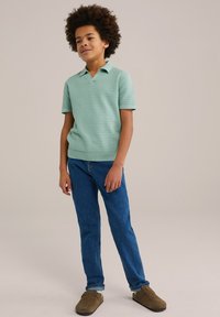 Polo verde claro de manga corta con un patr�ón texturizado, combinado con jeans azules y calzado marrón. El estilo es casual y cómodo.