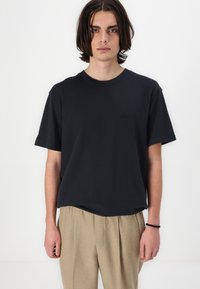 Camiseta de algodón negra con mangas cortas, corte relajado y cuello redondo. Presenta un logotipo en relieve en la parte delantera.