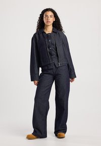 Donkerblauw gestreept tweedelig ensemble bestaande uit een cropped jasje en wijde broek, gemaakt van een gestructureerde stof met knoopdetails.