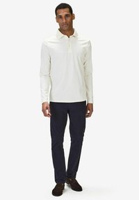 Pitkähihaista kermaista polo-takkia, puuvillamateriaalia, klassinen kaulus, yhdistetty tummiin slim-fit-housuihin ja ruskeisiin mokkanahkakenkiin. Yksinkertainen muotoilu, ei kuvioita.