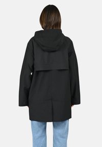 Giacca nera con cappuccio dal design strutturato, ampio pannello posteriore e dettagli con bottoni. Il materiale sembra liscio e resistente.