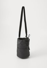 Zwarte stoffen schoudertas met een cilindervorm, verstelbare schouderriem, trekkoordsluiting en een zijvak. Gladde textuur met minimale accenten.
