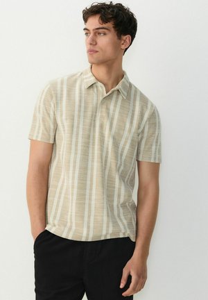 Kortærmet polo-shirt i beige med subtile lodrette striber. Har en spids krave og struktureret stof. Bæres med sorte bukser.