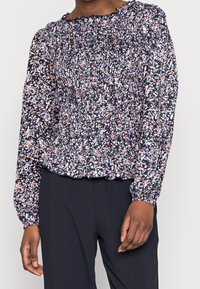 Maglia a maniche lunghe di colore blu navy con motivo floreale in rosa, viola e blu. Presenta un design arricciato nel corpetto e un orlo arruffato.