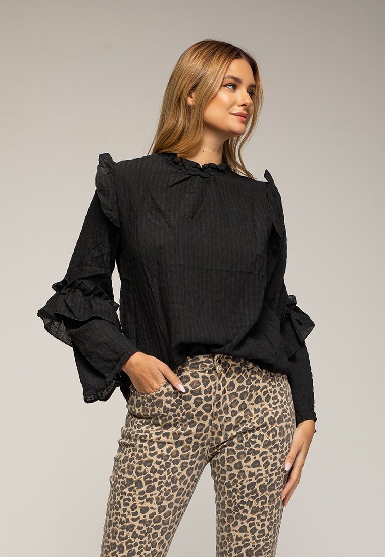 Schwarze Bluse mit strukturiertem Material, Rüschensleeves und hohem Kragen, kombiniert mit einer figurschmeichelnden Hose im Leopardenmuster mit Taschen.