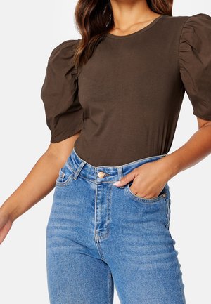 Brązowy dopasowany top z bufkami, zestawiony z niebieskimi dżinsami o wysokim stanie, z przodem na guzik i tradycyjnym pięciopocketowym fasonem.