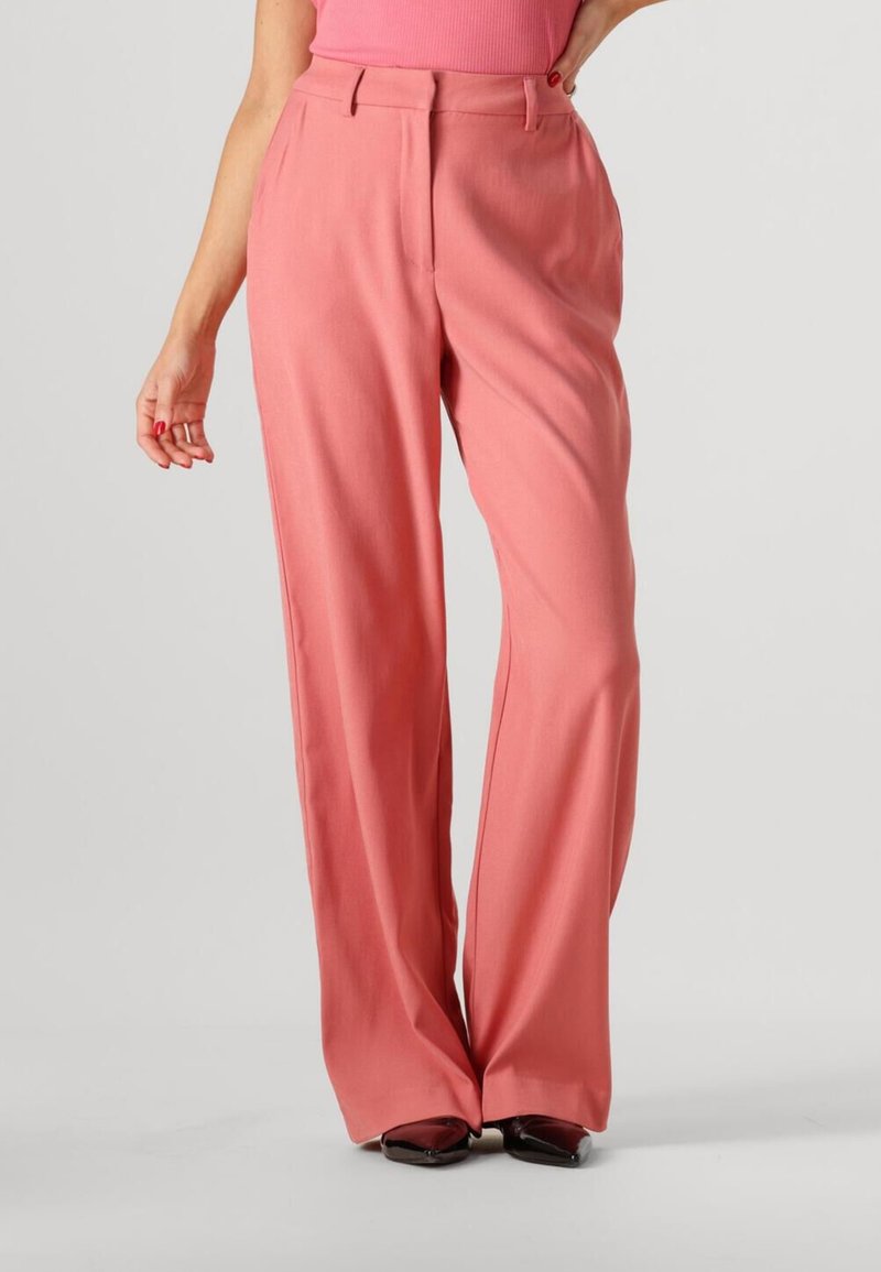 Roze wijde broek van gladde stof met een getailleerde pasvorm; beschikt over plooien en een hoge tailleband, gecombineerd met donkere schoenen.