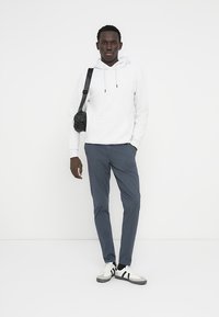 Λευκό φούτερ με κουκούλα, σκούρο μπλε παντελόνι με στενή γραμμή, μαύρη τσάντα χιαστί και λευκά αθλητικά παπούτσια με μαύρες ρίγες. Μινιμαλιστικό στυλ, απαλά υφάσματα.