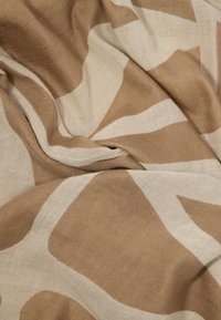 Beige og lys brunt stoff med geometriske former, vist rynket og brettet for å fremheve tekstur og mønster.