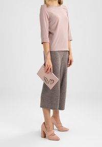 Hellrosa Dreiviertelarm-Oberteil, graue gerippte Culottes, rosa Pumps mit Absatz und eine passende Clutch mit Lippen- und Herzdesigns.