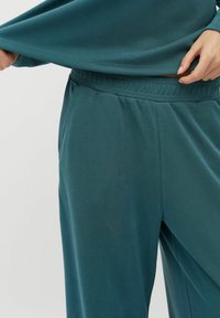 Teal loungewear set met een longsleeve top en broek met elastische tailleband, gemaakt van een zachte, gladde stof, met een relaxte pasvorm.