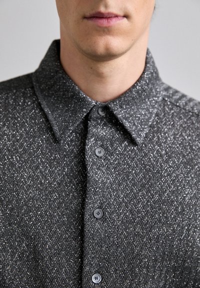Camisa gris de espiga hecha de tejido texturizado. Presenta un cuello, siete botones en la parte delantera y un sutil detalle metálico en todo su diseño.