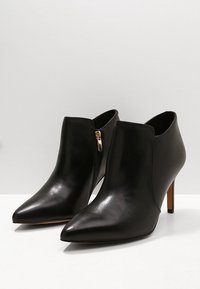 Stivaletti neri in pelle con punte appuntite, cerniere laterali e tacchi a spillo. Texture liscia con finitura lucida e accenti minimi.