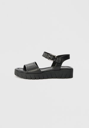 Black leather sandal with a wide strap over the toes, ankle strap with a buckle, and thick notched sole for support.