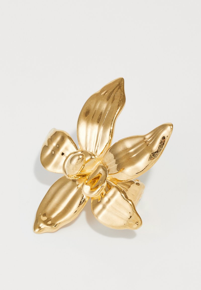 Gullfarget blomsterformet ring med fire teksturerte kronblader, en glatt midtseksjon og en polert overflate som reflekterer lys.