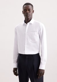 Witte lange mouwen shirt met een button-down kraag en een borstzak, gecombineerd met donkere broek, met een gladde textuur en een getailleerde pasvorm.