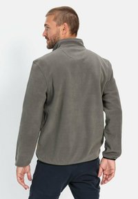 Fleecejakke i grå med høj krave, som har lange ærmer og en glat overflade. Hæmmen har en let kurve; inkluderer en lille logomærkat.