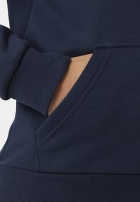 Felpa blu navy con tasca a marsupio, polsini a coste e una consistenza morbida. Il tessuto è liscio, con una trama uniforme e cuciture nette.