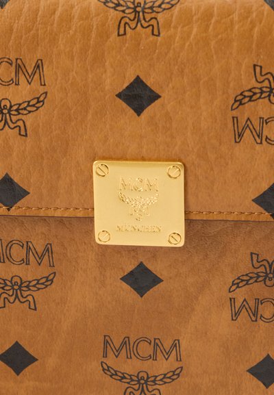Καφέ δερμάτινη τσάντα με μαύρα λογότυπα MCM και ένα χρυσό τετράγωνο μεταλλικό στοιχείο με χαραγμένο κείμενο. Υφή με ορατή ραφή.