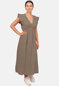 Robe longue, marron, texturée avec un décolleté en V profond et des manches volantes, assortie à des baskets blanches. La robe a un corsage ajusté et une jupe fluide.
