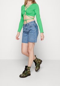 Zielony długi rękaw crop top z krzyżowym wzorem, połączony z wysokimi dżinsowymi szortami i czarnymi bojówkami we wzór kwiatowy.