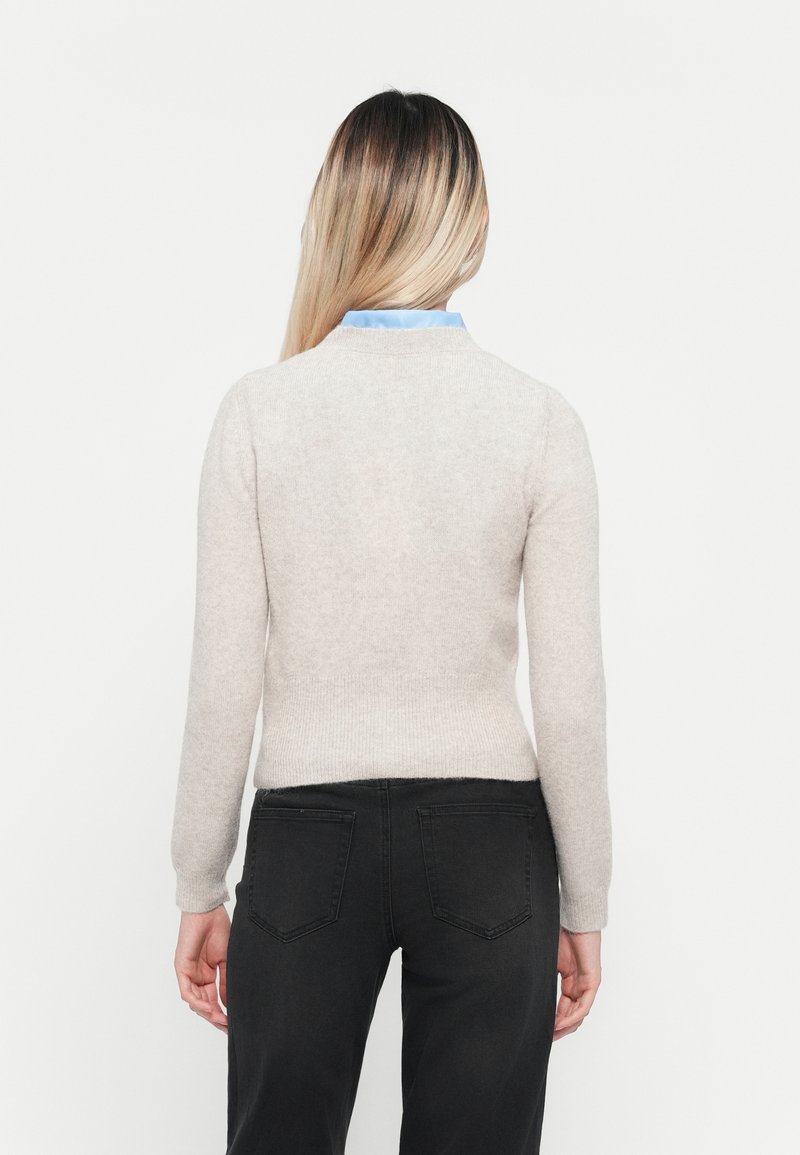 Helle beige Pullover mit Rundhalsausschnitt und gerippten Bündchen. Kombiniert mit dunklen Jeans, die eine glatte Textur und eine taillierte Passform zeigen.
