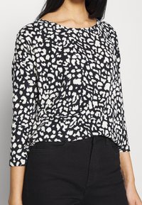 Svart och vit långärmad topp med ett leopardsmönster, med vid halsringning och en avslappnad passform. Tyget verkar mjukt och strukturerat.