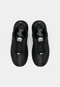 Ζευγάρι μαύρα αθλητικά παπούτσια της μάρκας Buffalo με κορδόνια, εμφανές λογότυπο στη γλώσσα και στην εσωτερική σόλα, σε θέα από πάνω σε λευκό φόντο.